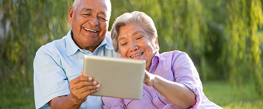 Senior couple laughing while looking at a tablet outside