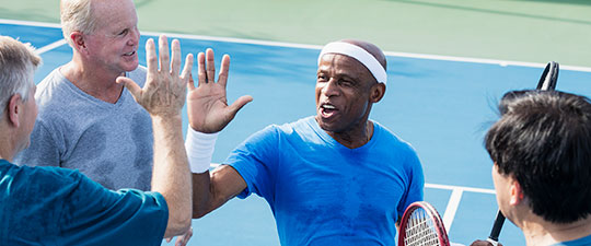 Senior men standing at tennis net trade high-5s after a tennis match