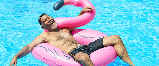 Senior man floating in the pool with a flamingo floatie