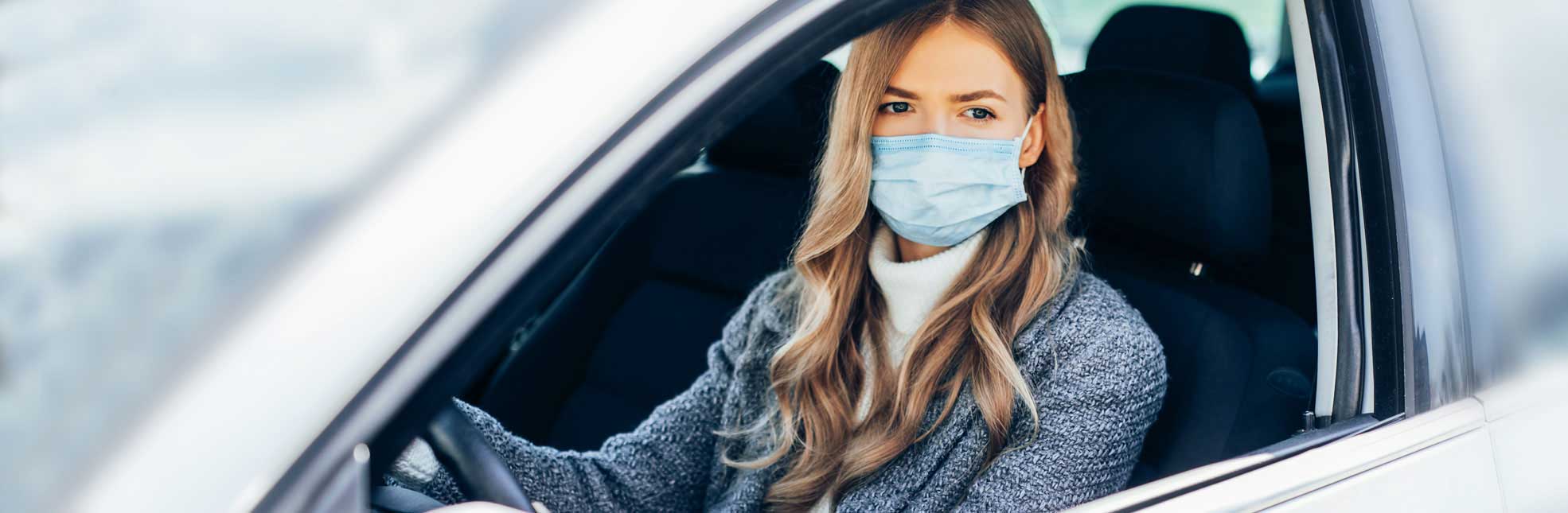 young woman driving a car with a mask on