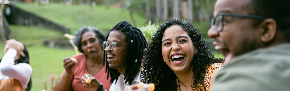 Group of four friends laughing together while outside eating orange slices
